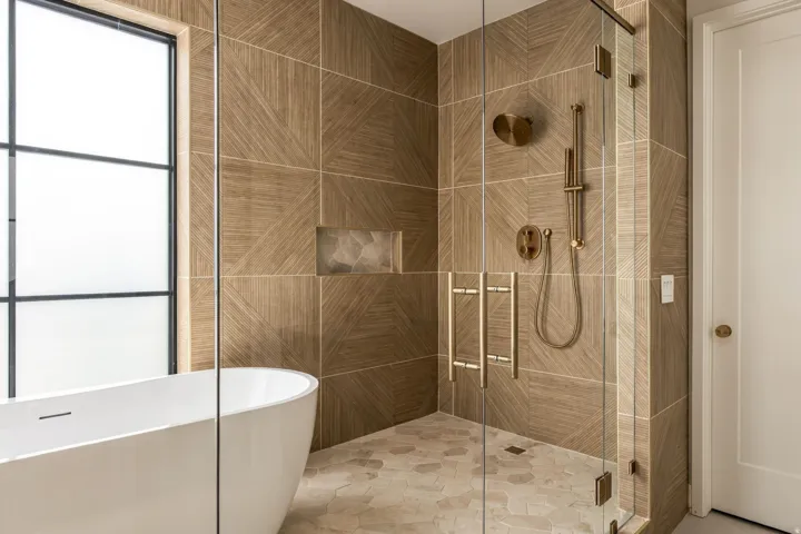 Freestanding soaking tub, walk-in shower with glass enclosure, mosaic-tiled shower floor, and brushed brass fixtures