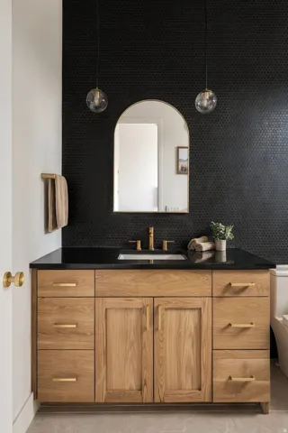 Custom vanity with wood finish, black countertop, integrated sink, and brass-finish hardware