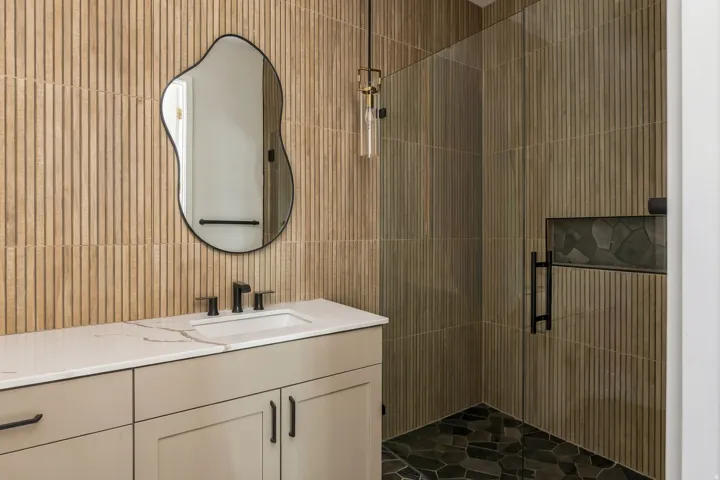 Vanity with integrated sink, stone countertop, matte black fixtures, and a frameless shower with dark stone-finish flooring