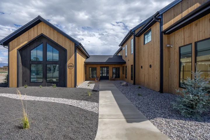 Gable roofline with large framed windows, natural wood-finish siding, black trim details, and a concrete pathway