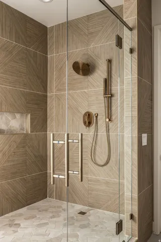 Glass-enclosed shower featuring large format wall tiles, a built-in shower niche, and a contrasting hexagonal floor tile