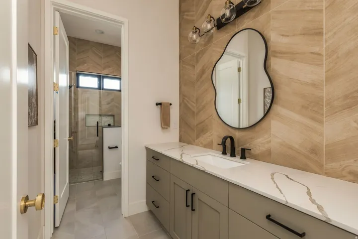 Extended vanity with a white countertop and integrated sink, chevron-patterned wall tile, and a walk-in shower with a glass enclosure