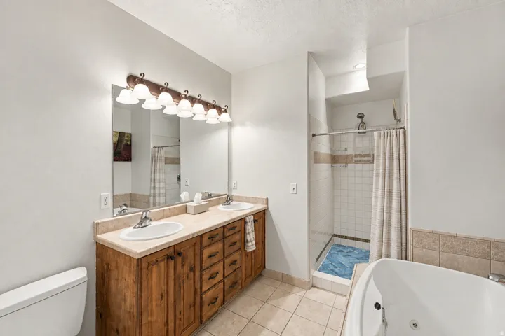 Dual vanity with wood-finish cabinetry, built-in soaking tub, and a separate shower with tiled walls