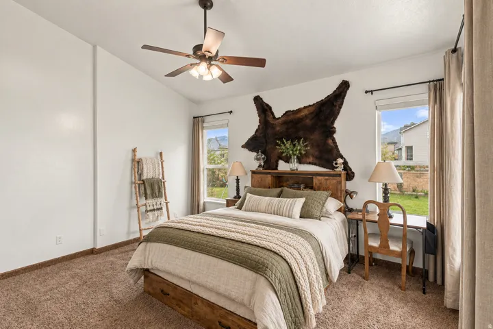 Vaulted ceiling with a ceiling fan, plush carpet flooring, and dual windows with curtains