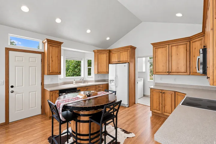 Kitchen featuring vaulted ceilings, wood-finish flooring, wood cabinetry, light countertops, and recessed lighting