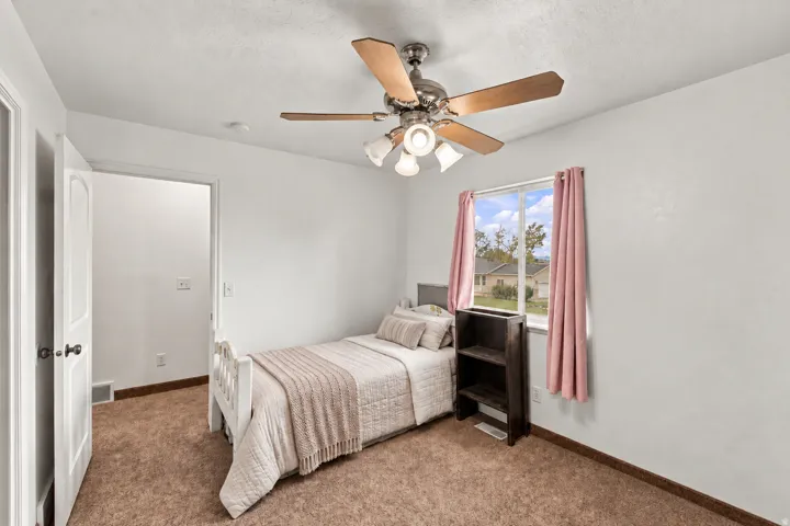 Recessed window with white trim, ceiling fan with light fixture, white interior door with dark hardware, and brown carpet flooring