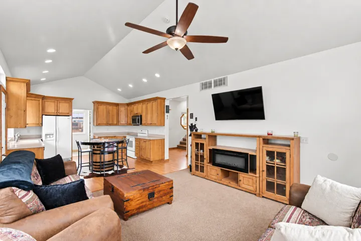 Vaulted ceilings with recessed lighting, wood-finish cabinetry, a ceiling fan with integrated lighting, and a built-in media console with an electric fireplace