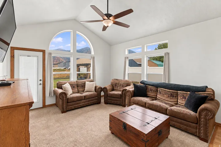 Vaulted ceiling with a ceiling fan, carpeted flooring, and a glass-paneled exterior door