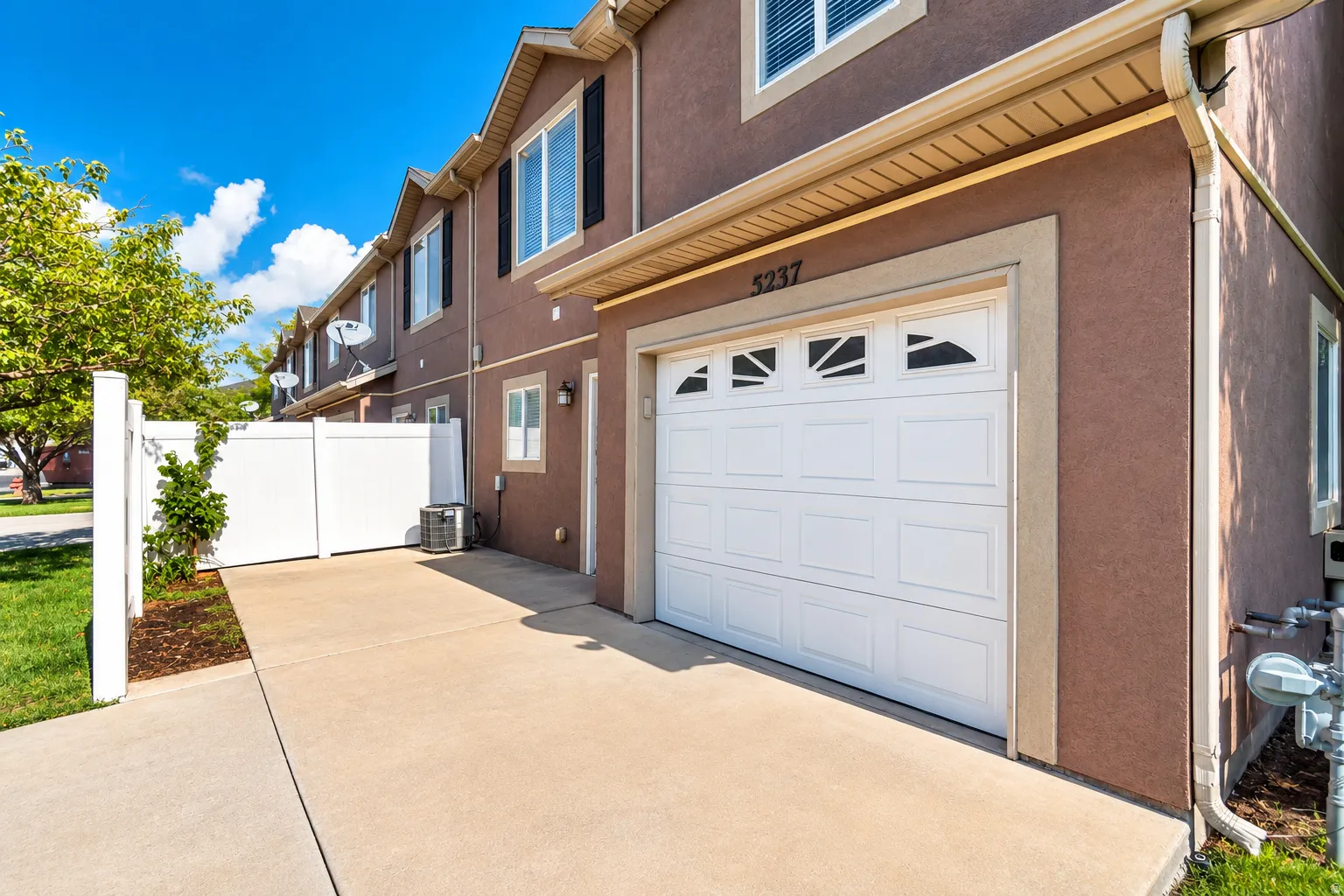Stucco exterior, white garage door with decorative windows, concrete driveway, and white vinyl fencing