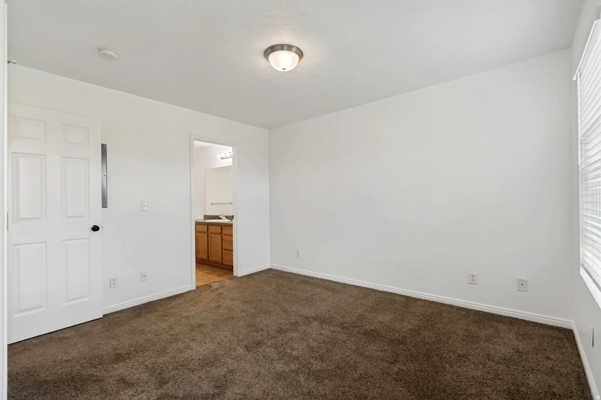 Carpeted room with white walls, a flush-mount ceiling light, and a window with horizontal blinds