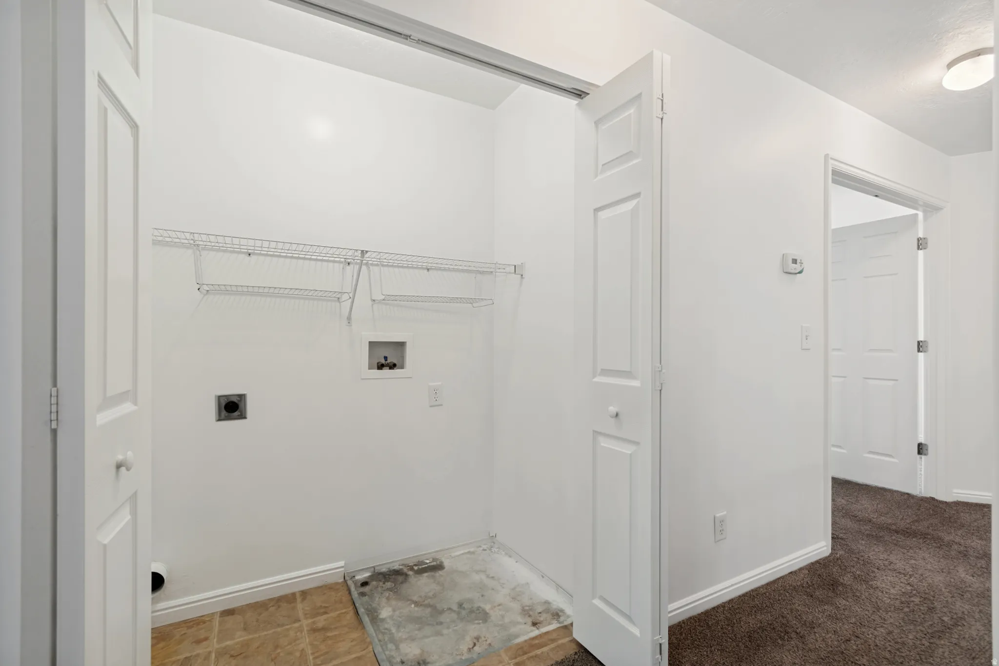 Dedicated laundry closet featuring wire shelving, utility hookups, and a bi-fold door
