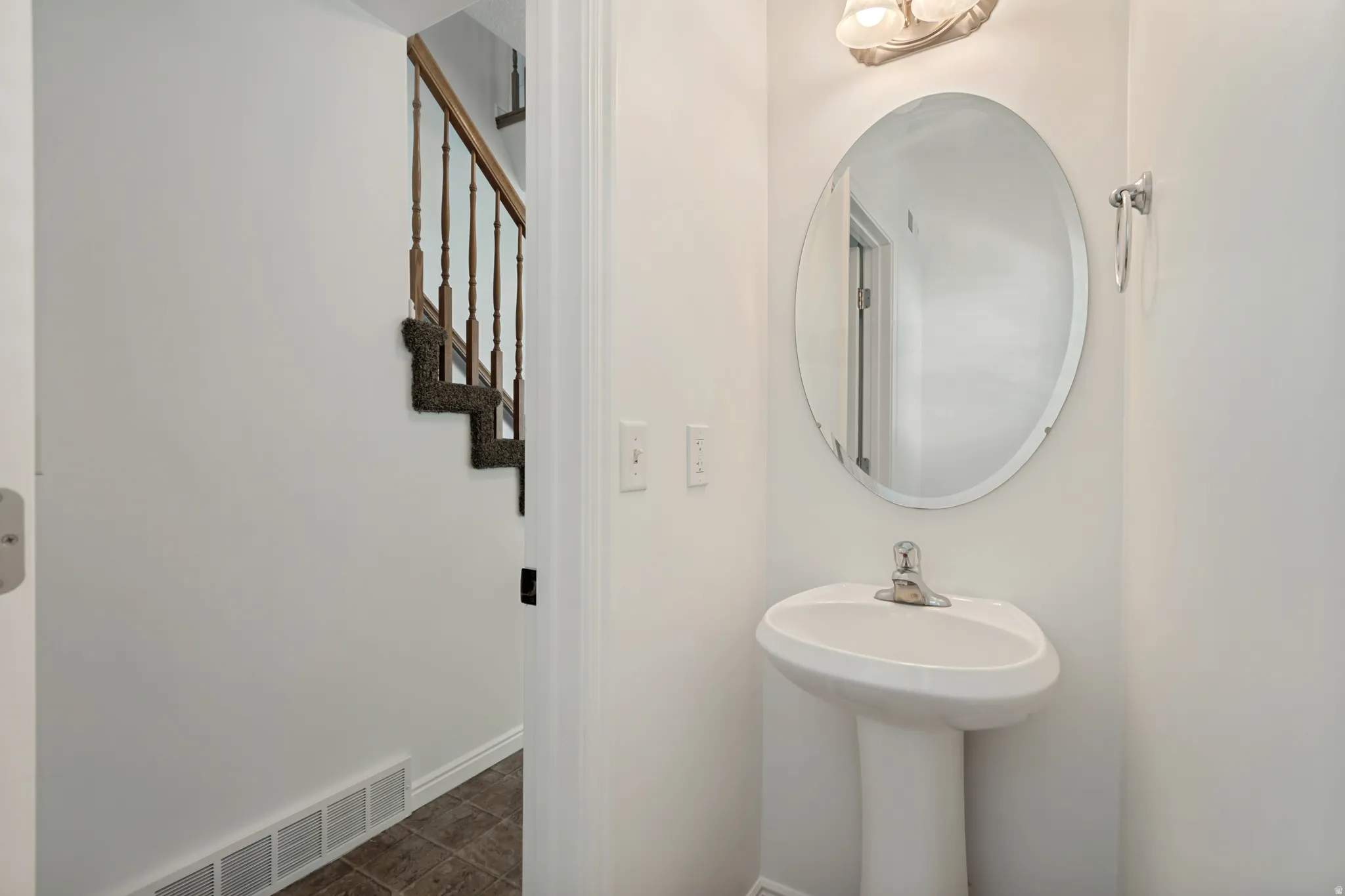 Pedestal sink with single-handle faucet, oval mirror, and wall-mounted vanity light