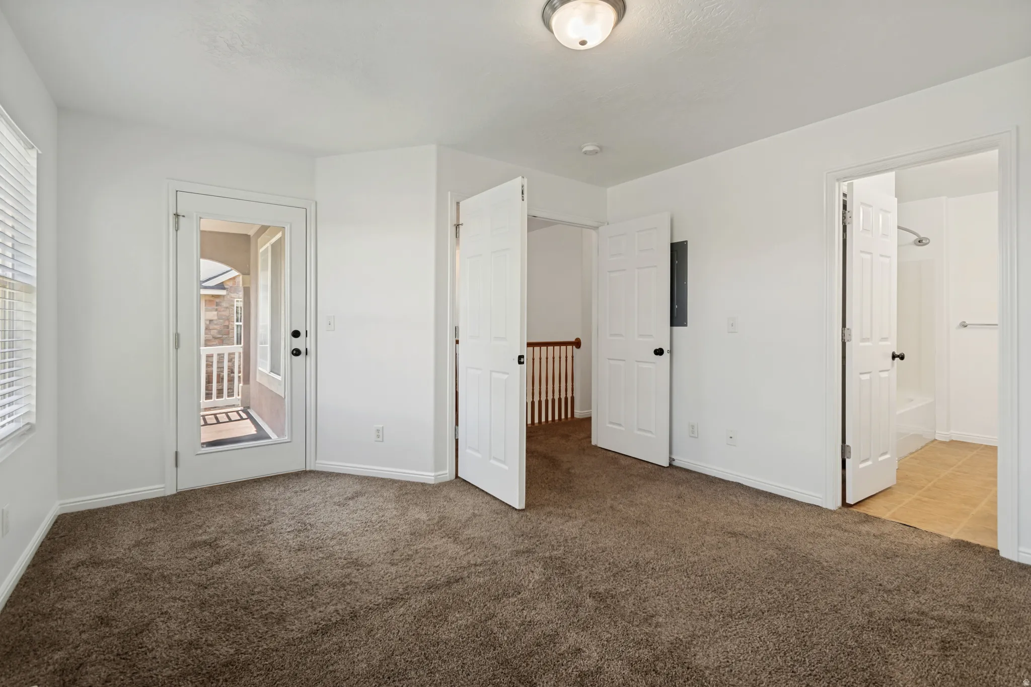 Carpeted room with white walls, a glass-paneled door leading to an exterior balcony, and a window with blinds