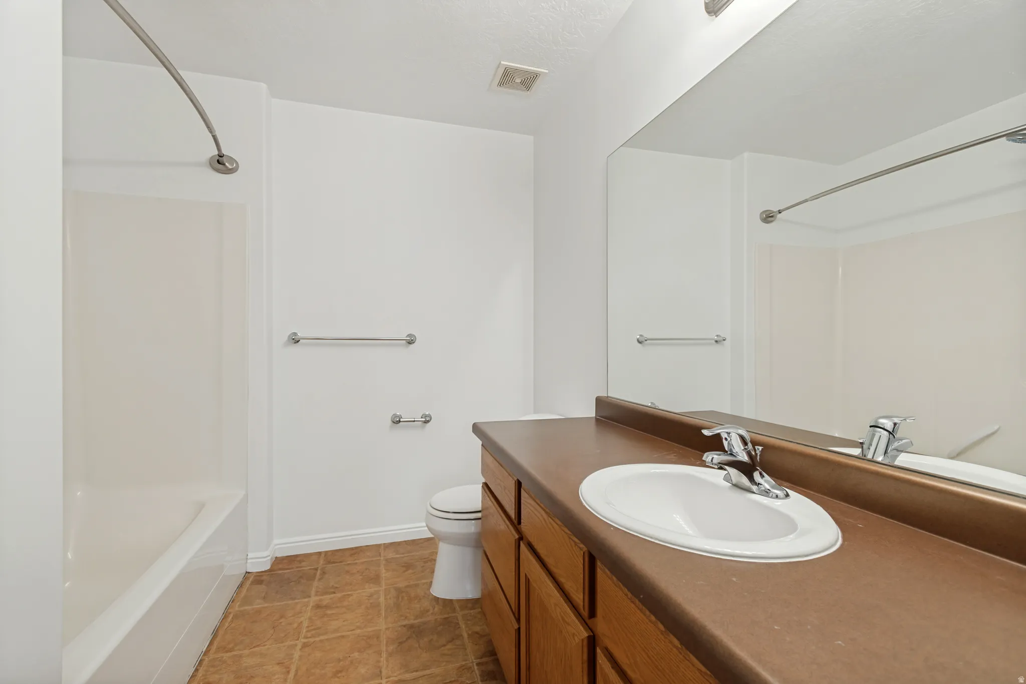 White bathtub with shower, wood-finish vanity with integrated sink, chrome faucet, and expansive wall mirror