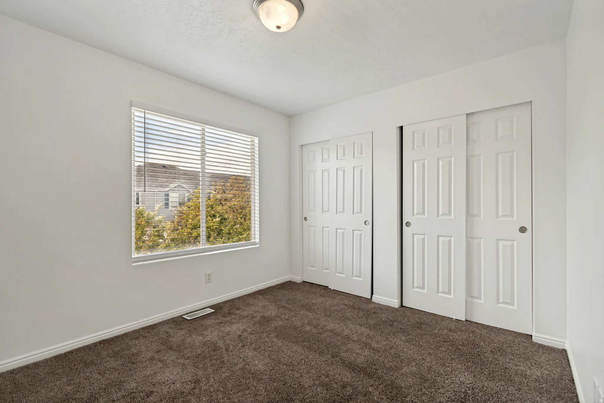 Neutral white wall paint, brown carpet flooring, and two sets of sliding closet doors