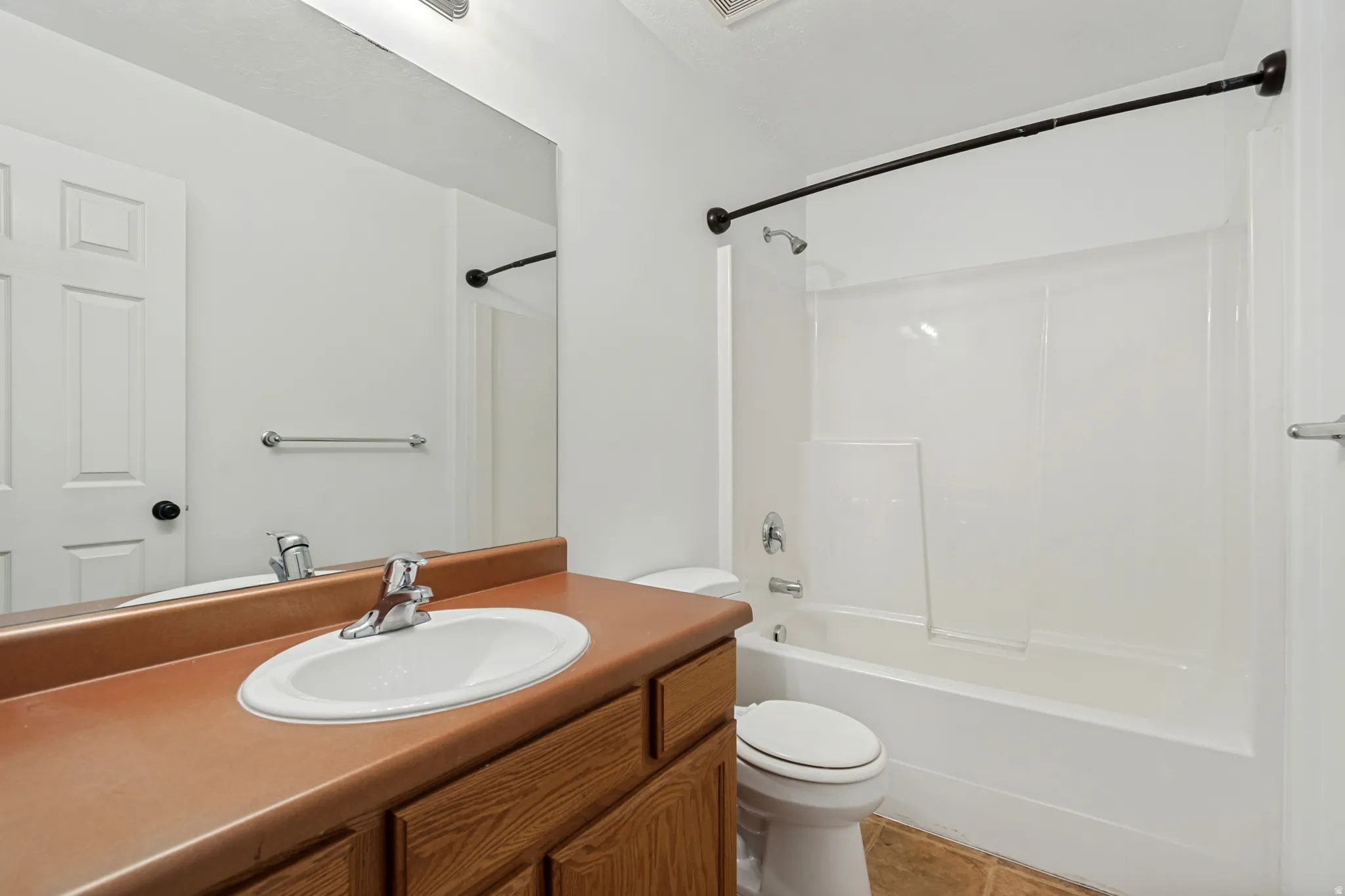 Bathroom featuring a single vanity with wood-finish cabinetry, a large wall-mounted mirror, a toilet, and a combined shower and tub with a white surround