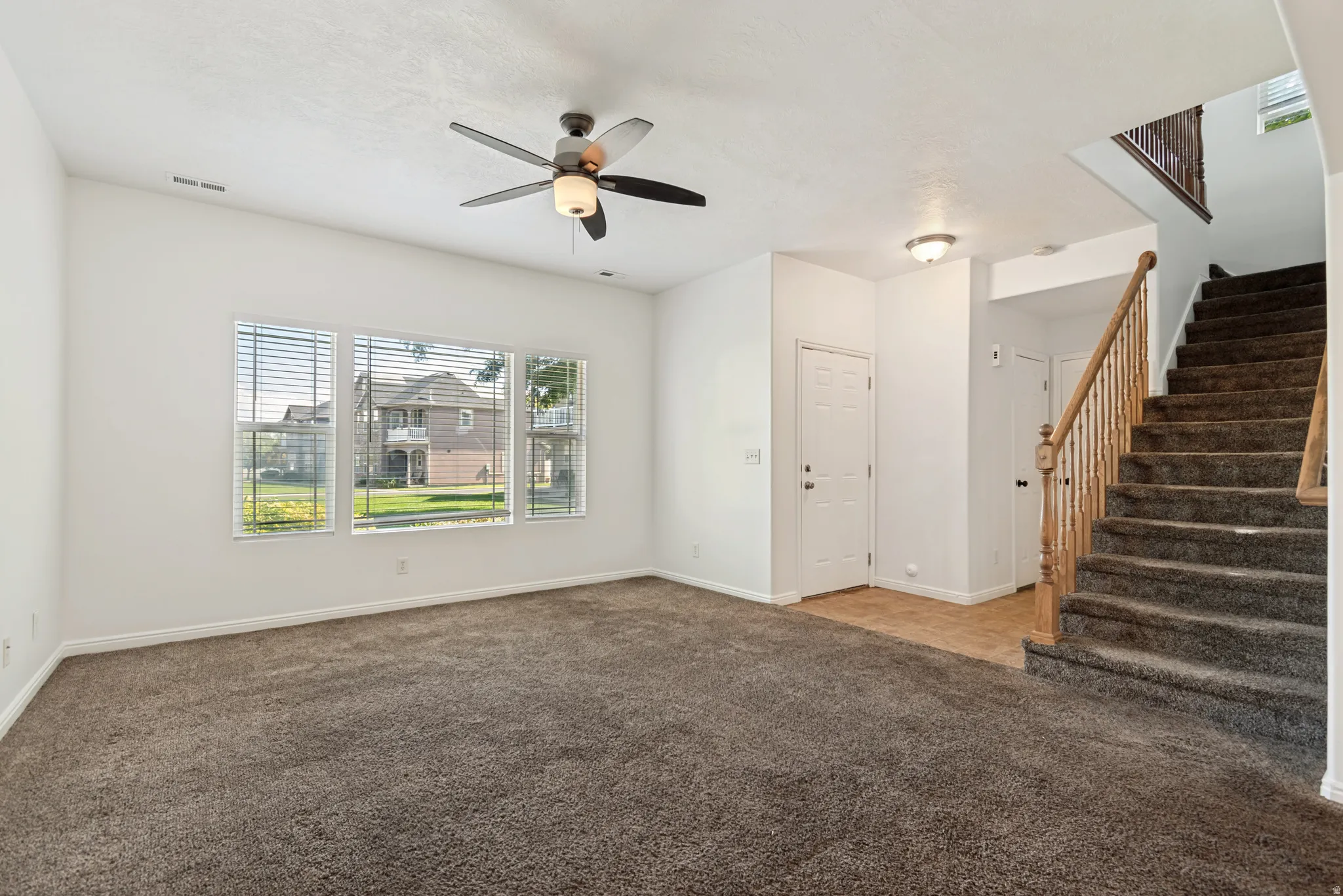 Three large windows, ceiling fan with integrated lighting, wood-finish staircase railing, and carpeted stairs