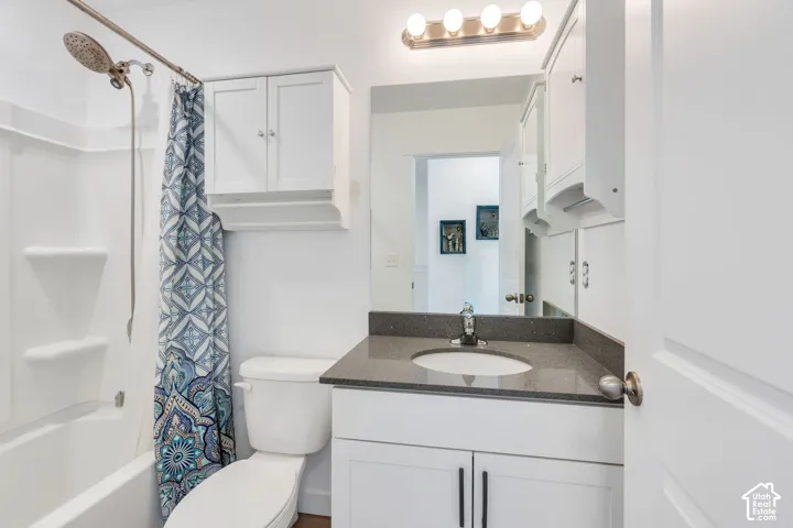White vanity with a dark countertop and integrated sink, chrome faucet, and overhead lighting