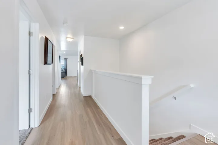 View from front door. Wide front hallway.  Light wood-finish flooring extending through the hallway, white painted walls, white trim, recessed lighting, and a white staircase with a half-wall railing