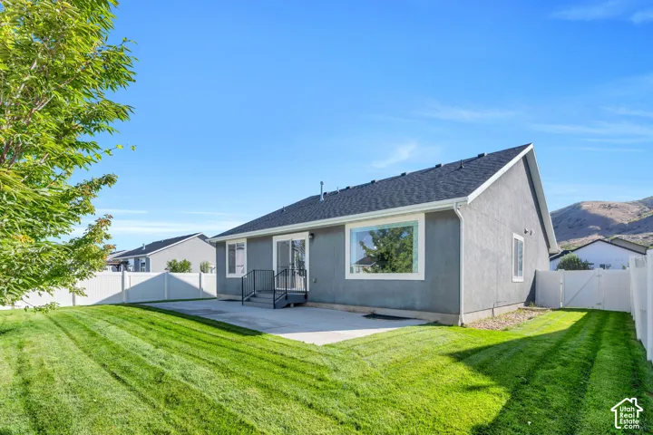 Expansive backyard featuring a concrete patio, sliding glass door access, white vinyl fencing, and a manicured lawn