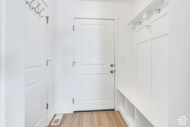 At garage entrance. Built-in mudroom bench with storage cubbies and wall hooks, wood-finish flooring, and white paneled doors