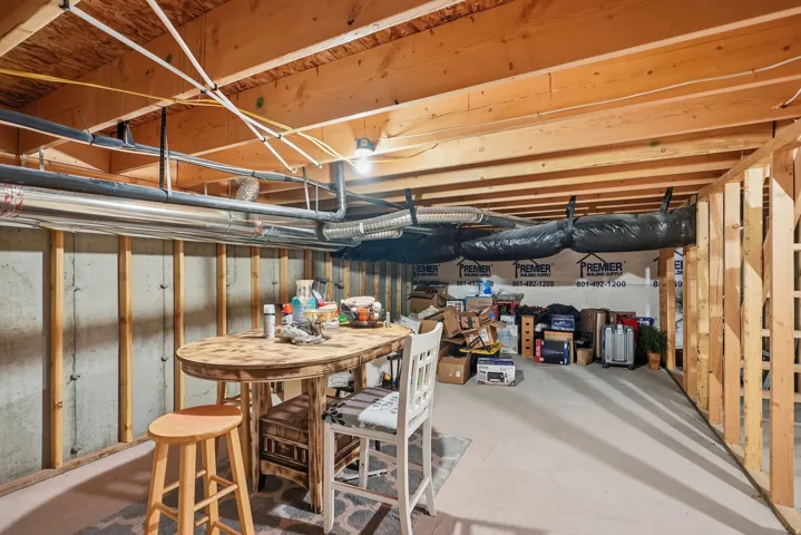 Unfinished basement with exposed wood framing, concrete walls, and overhead utility lines