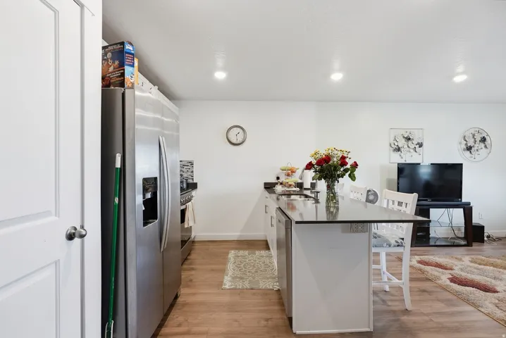Stainless steel appliances, recessed lighting, wood-finish flooring, white cabinetry, and a center island with sink
