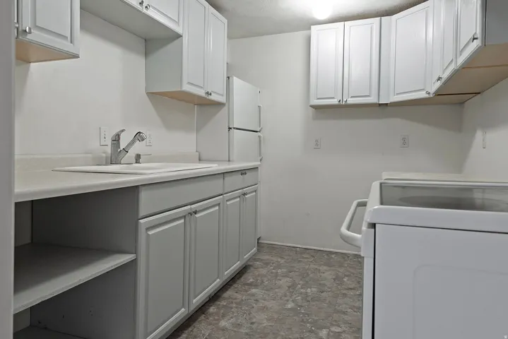 Kitchenette featuring white cabinetry, a stainless steel faucet with a pull-down sprayer, a white sink, and light-toned countertops