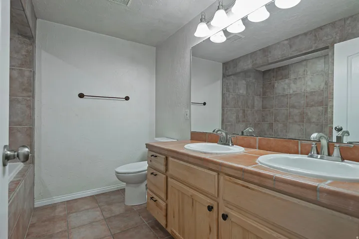 Dual undermount sinks with chrome fixtures, wood vanity cabinetry, large wall-mounted mirror, and tile flooring