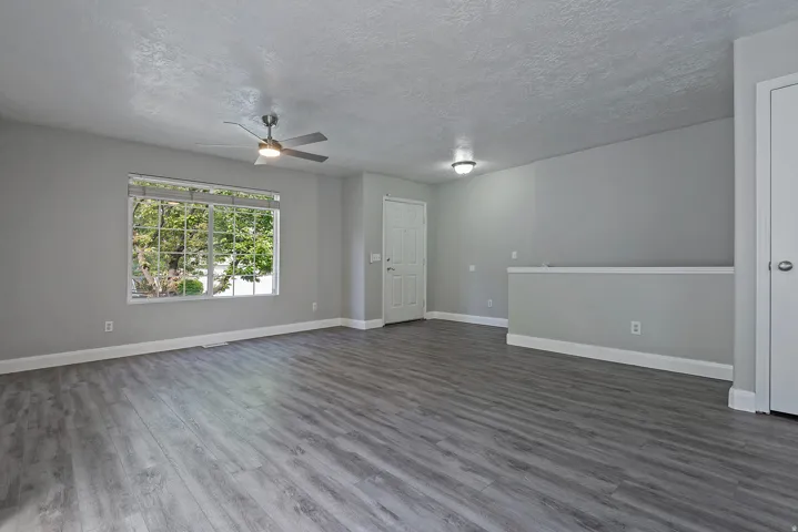 Spacious room featuring wood-finish flooring, a large window, ceiling fan, and modern flush-mount lighting