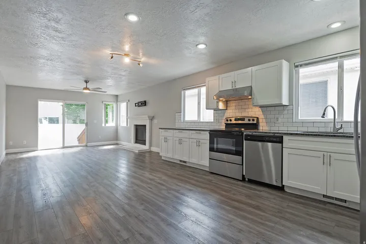 Open-concept living area with wood-finish flooring, white shaker cabinetry, stainless steel appliances, and a tiled kitchen backsplash