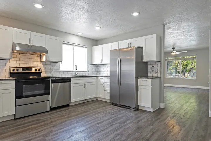 Modern kitchen featuring white cabinetry, stainless steel appliances, a subway tile backsplash, and dark countertops