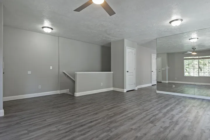 Spacious room featuring wood-finish flooring, ceiling fan, and mirrored wall