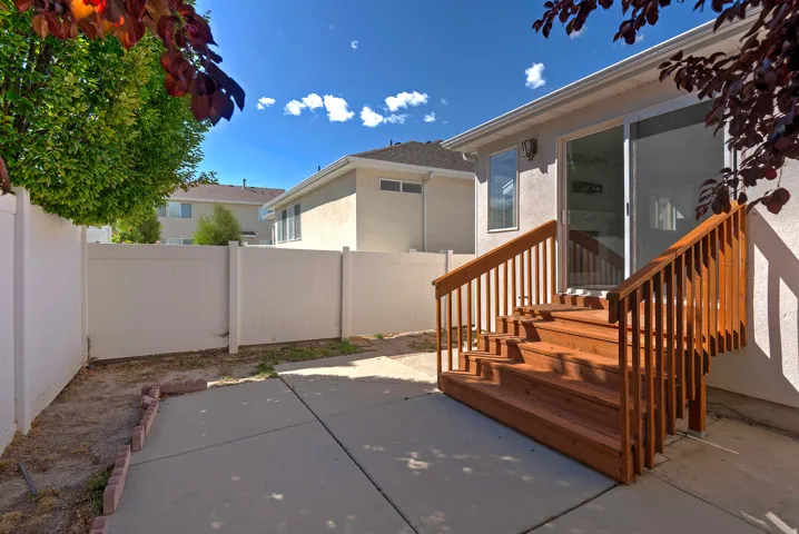 Concrete patio with red-toned wood stairs, white perimeter fencing, and a glass sliding door
