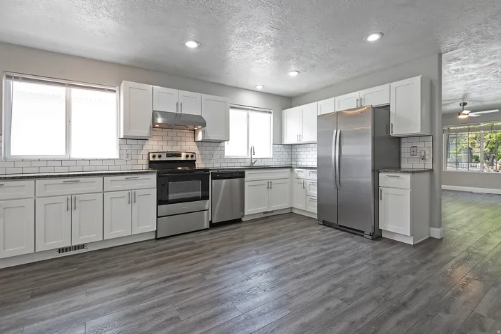 Kitchen with white shaker cabinetry, dark countertops, white subway tile backsplash, stainless steel appliances, and wood-finish flooring