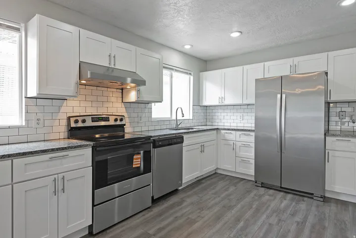 Contemporary kitchen featuring white shaker cabinetry, stainless steel appliances, a subway tile backsplash, granite-style countertops, and wood-finish flooring