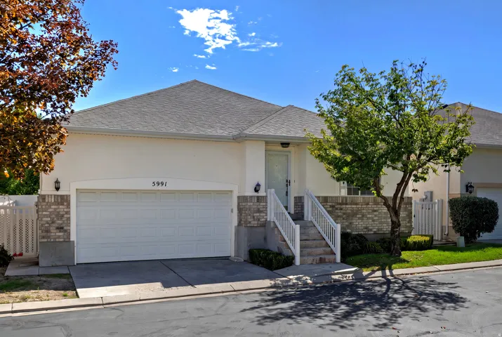 Stucco exterior with brick accents, attached garage, concrete driveway, and front entry with steps and railings