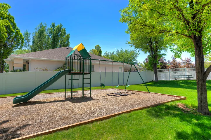 Playground structure with slide and swings, surrounded by wood chip surfacing