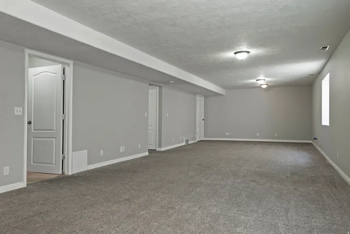 Expansive room featuring neutral wall tones, gray carpeting, multiple interior doors, and flush-mount ceiling lighting