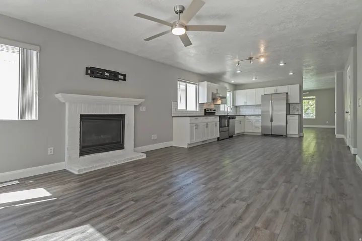 Open-concept living area featuring wood-finish flooring, a white brick fireplace, a ceiling fan, and recessed lighting