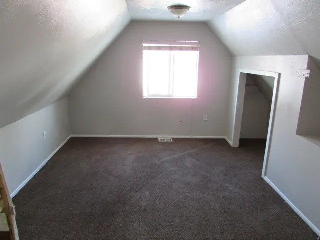 Sloped ceilings with recessed lighting, neutral wall paint, and a window with blinds