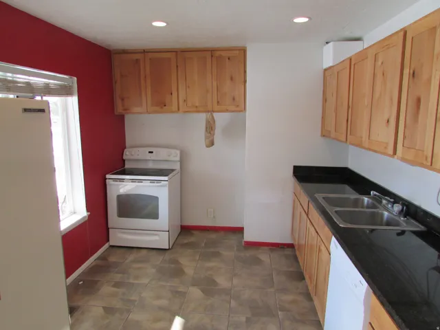 Kitchen featuring wood cabinetry, dark countertops, a double basin stainless steel sink, tile flooring, and recessed lighting