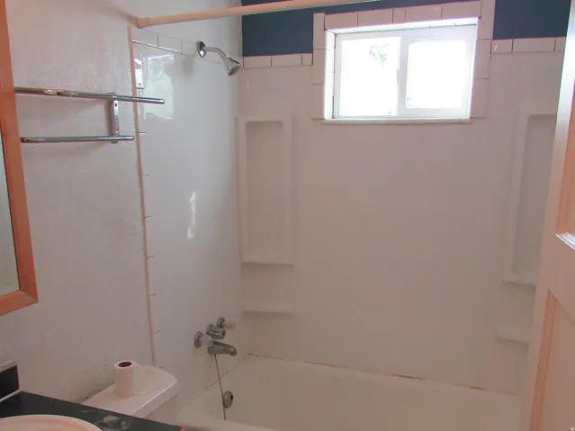 White bathtub with integrated shelving, a window, and a shower fixture
