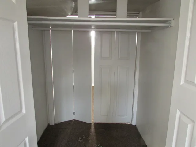 Wardrobe featuring bi-fold doors, white shelving, and a hanging rod