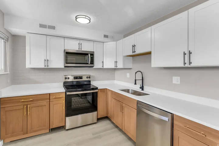 Updated kitchen featuring two-tone cabinetry, stainless steel appliances, a subway tile backsplash, white countertops, and wood-finish flooring