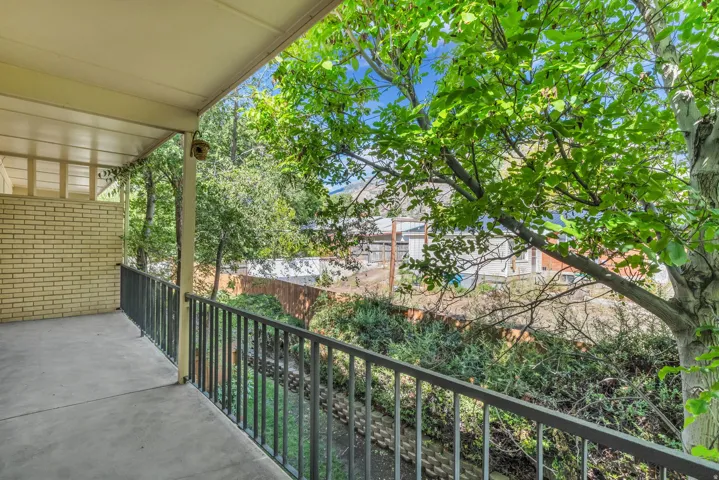 Covered balcony with concrete flooring, black metal railings, and a brick exterior wall