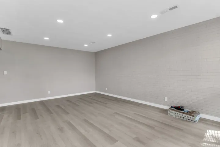 Recessed ceiling lighting, durable wood-finish flooring, and a whitewashed brick accent wall