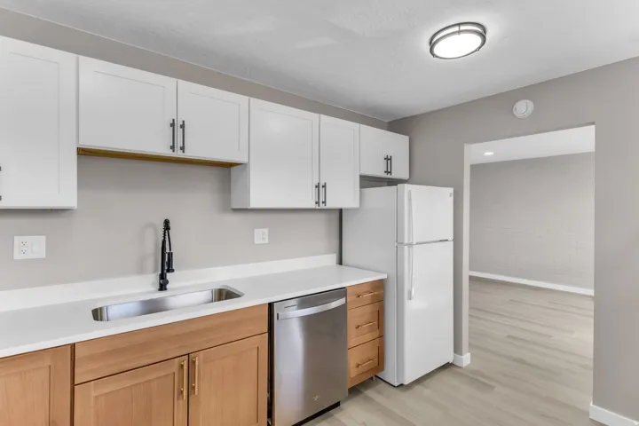 Kitchen featuring white upper cabinetry, wood-finish lower cabinetry, a stainless steel sink, and light-toned countertops