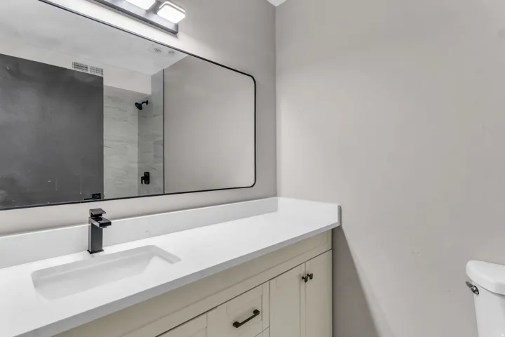 White countertop with an integrated rectangular sink, matte black faucet, and a large wall-mounted mirror