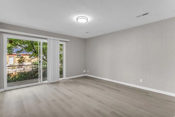 Wood-finish plank flooring, painted brick accent wall, flush-mount ceiling light, white sliding glass door, and exterior metal railing